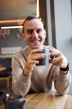 Yakışıklı, gülümseyen, sakin bir genç adam bir kafede bir restoranda bir masada otururken kahve içer. Sabah kahvesi