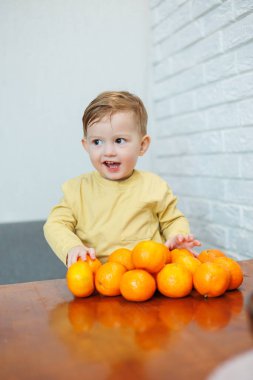 2 yaşında küçük bir çocuk mandalinaları elinde tutuyor. Çocuk ilk kez turunçgillerin üzerine oturmak istiyor..
