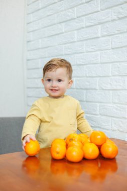 İki yaşında küçük bir çocuk mandalinalarla dolu bir masada duruyor. Bebek ilk kez narenciye yemek istiyor.