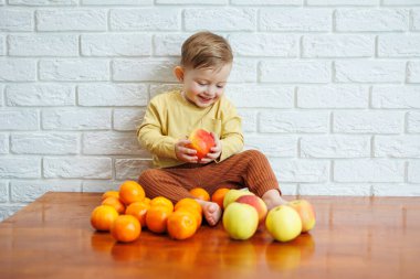 Tatlı gülümseyen çocuk taze, sulu bir kırmızı elma yiyor. Küçük çocuklar için sağlıklı meyveler