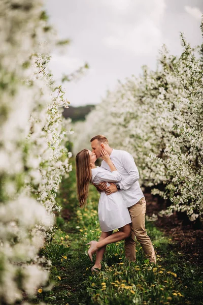 美丽的年轻夫妇在一个浪漫的地方 春天盛开的苹果园 这对快乐的夫妇在花园里散步时彼此快乐 男人牵着女人的手 — 图库照片