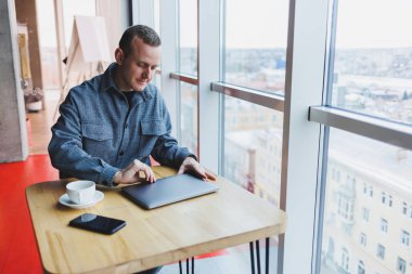 Takım elbiseli başarılı genç bir işadamı kahve içer ve bir kafede kablosuz internet üzerinden bir laptopta tek başına bir kafede oturur..