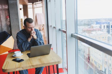 Takım elbiseli başarılı genç bir işadamı kahve içer ve bir kafede kablosuz internet üzerinden bir laptopta tek başına bir kafede oturur..