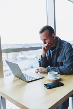 Takım elbiseli başarılı genç bir işadamı kahve içer ve bir kafede kablosuz internet üzerinden bir laptopta tek başına bir kafede oturur..