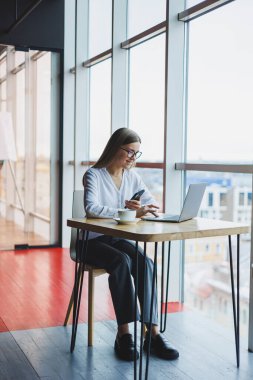 Akıllı bir kadın yönetici bir fincan kahveyle akıllı bir telefonla teslimat siparişini tartışır, genç bir kadın küçük sahibi bir kafede dizüstü bilgisayarla oturur ve aramalar yapar.