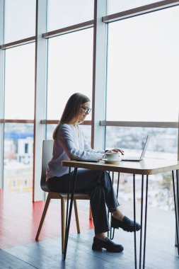 Çekici, açık renk elbiseli ve gözlüklü bir kadın bir kafede kahve içerken dizüstü bilgisayara konsantre oluyor ve daktilo çekiyor. Beyaz gömlekli ve gözlüklü bir kız öğrenci.