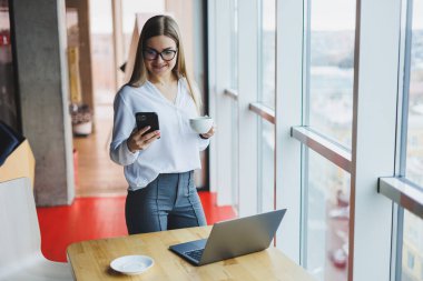 Genç ve güzel bir kadın kafede oturmuş konuşurken gülüyor, sipariş veriyor ve dizüstü bilgisayarına not alıyor. Kahve içerken cep telefonundan arayan pozitif kız.