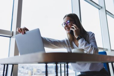 Genç ve güzel bir kadın kafede oturmuş konuşurken gülüyor, sipariş veriyor ve dizüstü bilgisayarına not alıyor. Kahve içerken cep telefonundan arayan pozitif kız.