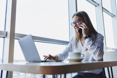Genç ve güzel bir kadın kafede oturmuş konuşurken gülüyor, sipariş veriyor ve dizüstü bilgisayarına not alıyor. Kahve içerken cep telefonundan arayan pozitif kız.