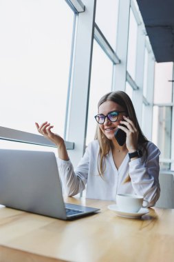 Genç ve güzel bir kadın kafede oturmuş konuşurken gülüyor, sipariş veriyor ve dizüstü bilgisayarına not alıyor. Kahve içerken cep telefonundan arayan pozitif kız.