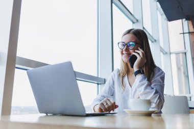 Genç ve güzel bir kadın kafede oturmuş konuşurken gülüyor, sipariş veriyor ve dizüstü bilgisayarına not alıyor. Kahve içerken cep telefonundan arayan pozitif kız.