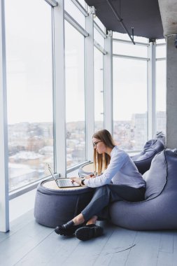 Bir iş kadını elinde dizüstü bilgisayarla bir kafede oturan ekrana bakar. Not defterine not alır. Dizüstü bilgisayara bakar.