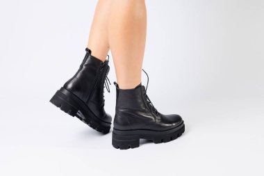 Beyaz arka planda modaya uygun siyah ayakkabılı bir kadın, yakın plan. Şık deri ayakkabılı kadın bacakları.