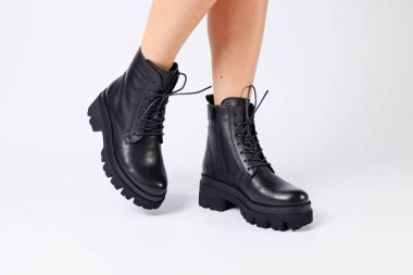 Beyaz arka planda modaya uygun siyah ayakkabılı bir kadın, yakın plan. Şık deri ayakkabılı kadın bacakları.