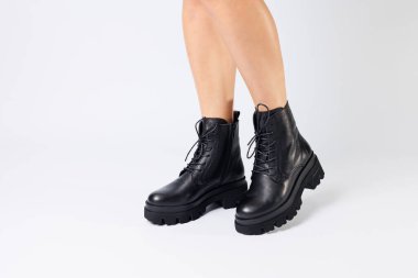 Beyaz arka planda modaya uygun siyah ayakkabılı bir kadın, yakın plan. Şık deri ayakkabılı kadın bacakları.