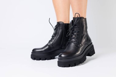 Beyaz arka planda modaya uygun siyah ayakkabılı bir kadın, yakın plan. Şık deri ayakkabılı kadın bacakları.