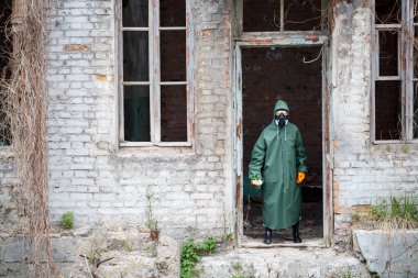 Koruyucu giysiler içinde bir dozimetrist bilim adamı ve gaz maskesi tehlike bölgesini inceliyor. Yakın plan. Çiçek ellerinde.