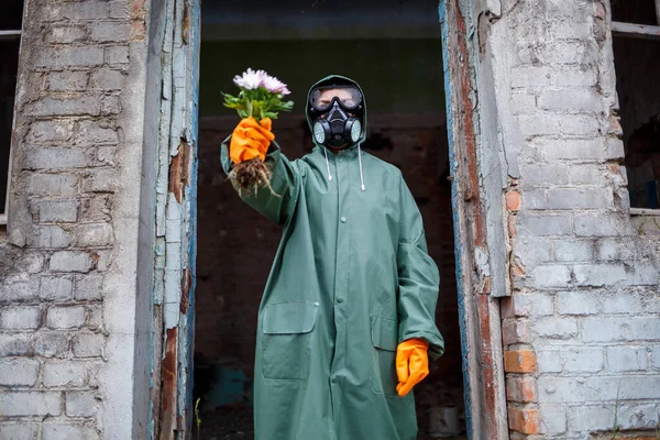 A dosimetrist scientist in protective clothing and a gas mask examines the danger zone. Close-up. flower in hands