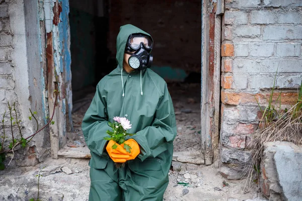 A dosimetrist scientist in protective clothing and a gas mask examines the danger zone. Close-up. flower in hands