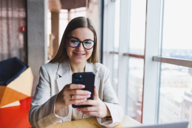 Gülümseyen kadın yönetici, kafedeki 4G kablosuz ağına bağlanan çevrimiçi uygulama üzerinden çalışmak için cep telefonu dijital aygıtı kullanıyor, neşeli serbest çalışan