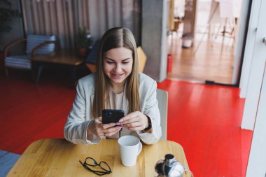 Gülümseyen kadın yönetici, kafedeki 4G kablosuz ağına bağlanan çevrimiçi uygulama üzerinden çalışmak için cep telefonu dijital aygıtı kullanıyor, neşeli serbest çalışan