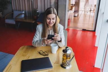 Genç ve güzel kadın işadamı akıllı telefonu iş için kullanıyor, online alışveriş, para transferi, finans, internet bankacılığı. Kafede çalışan bir kadın.
