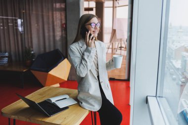 Genç ve çekici bir bayan yönetici boş zamanlarında bir kafede tek başına oturup bilgisayarla uğraşırken cep telefonuyla konuşuyor ve gülümsüyor. Mutlu kadın bir kafede dinleniyor..