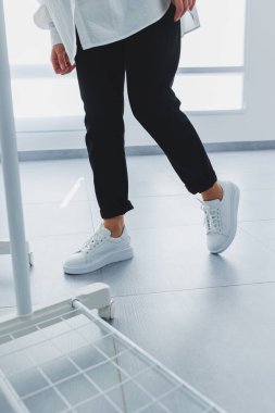 Siyah pantolonlu kadın bacakları ve beyaz deri spor ayakkabıları. Modern gündelik tarz. Yeni ayakkabı koleksiyonu
