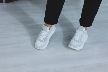 Bacaklı güzel kadın ayakkabıları, deri beyaz spor ayakkabılar, bir odanın içinde ya da ofiste, bir kadın için ayakkabılar, siyah pantolon ve beyaz spor ayakkabılar, gündelik ve modern tarz, modern ve moda