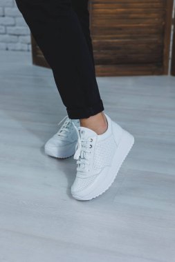 Bacaklı güzel kadın ayakkabıları, deri beyaz spor ayakkabılar, bir odanın içinde ya da ofiste, bir kadın için ayakkabılar, siyah pantolon ve beyaz spor ayakkabılar, gündelik ve modern tarz, modern ve moda