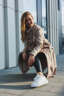 Güneşli bir günde asfaltta şık beyaz kadın deri ayakkabıları. Spor ayakkabılı kadın bacakları, trençkotlu kadın.