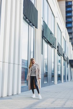 Güneşli bir günde asfaltta şık beyaz kadın deri ayakkabıları. Spor ayakkabılı kadın bacakları, trençkotlu kadın.