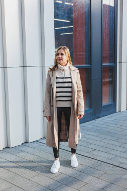 Güneşli bir günde asfaltta şık beyaz kadın deri ayakkabıları. Spor ayakkabılı kadın bacakları, trençkotlu kadın.