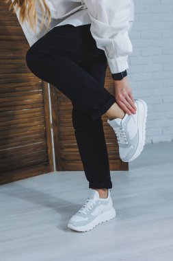 Siyah kotlu, şık, beyaz spor ayakkabılı kadın bacaklarının yakın çekimi. Yeni ayakkabılı şık bir kadın. Modern sezonluk şık spor ayakkabıları koleksiyonu. Kadın modası.