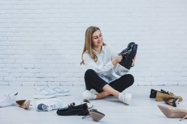 Yerde otururken şık bir sarışın ayakkabı seçiyor. Yerde bir sürü kadın ayakkabısı, şık bir ayakkabı seçimi..