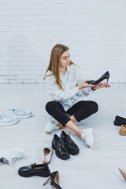 Yerde otururken şık bir sarışın ayakkabı seçiyor. Yerde bir sürü kadın ayakkabısı, şık bir ayakkabı seçimi..