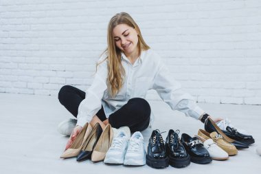 Yerde otururken şık bir sarışın ayakkabı seçiyor. Yerde bir sürü kadın ayakkabısı, şık bir ayakkabı seçimi..