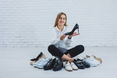 Yerde otururken şık bir sarışın ayakkabı seçiyor. Yerde bir sürü kadın ayakkabısı, şık bir ayakkabı seçimi..