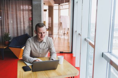 Bir web sitesinde bilgi arayan ve modern bir dizüstü bilgisayarda bir kafede kablosuz internet bağlantısı kullanarak bir grafik projesi geliştirmek için serbest çalışan zeki bir genç.