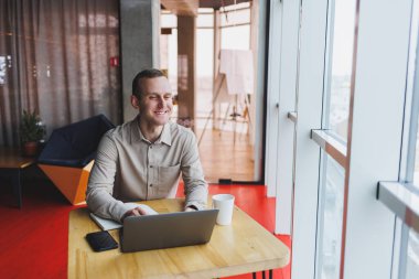 Bir web sitesinde bilgi arayan ve modern bir dizüstü bilgisayarda bir kafede kablosuz internet bağlantısı kullanarak bir grafik projesi geliştirmek için serbest çalışan zeki bir genç.