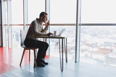 Bir web sitesinde bilgi arayan ve modern bir dizüstü bilgisayarda bir kafede kablosuz internet bağlantısı kullanarak bir grafik projesi geliştirmek için serbest çalışan zeki bir genç.