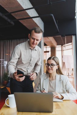 Bir iş projesinde birlikte çalışıyoruz. Modern büyük bir ofiste dizüstü bilgisayarla çalışan iki genç iş arkadaşı.