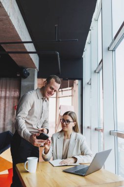İki farklı iş adamı büyük, modern bir ofiste otururken dizüstü bilgisayarla yeni bir proje üzerinde konuşuyor ve birlikte çalışıyorlar.