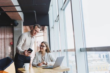 İki farklı iş adamı büyük, modern bir ofiste otururken dizüstü bilgisayarla yeni bir proje üzerinde konuşuyor ve birlikte çalışıyorlar.