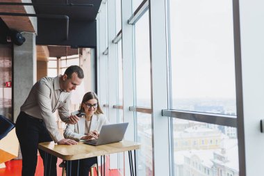 İki farklı iş adamı büyük, modern bir ofiste otururken dizüstü bilgisayarla yeni bir proje üzerinde konuşuyor ve birlikte çalışıyorlar.