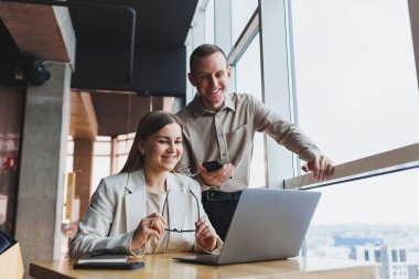 İki farklı iş adamı büyük, modern bir ofiste otururken dizüstü bilgisayarla yeni bir proje üzerinde konuşuyor ve birlikte çalışıyorlar.