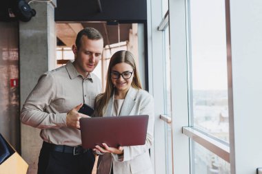 İki farklı iş adamı büyük, modern bir ofiste otururken dizüstü bilgisayarla yeni bir proje üzerinde konuşuyor ve birlikte çalışıyorlar.