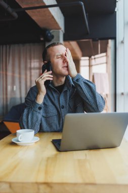 Uzaktan öğrenim sırasında internet tasarımı okuyan duygusal bir adam internetteki Wi-Fi 'ye bağlı internet araştırmaları için dizüstü bilgisayarda öğrenim görüyor. Telefon görüşmesi