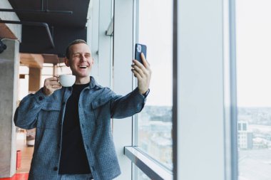 Avrupalı erkek serbest çalışan akıllı telefondan para transferlerini kontrol ediyor, internet üzerinden iş yapıyor, kafede uzaktan çalışıyor ve kahve içiyor.