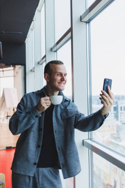 Avrupalı erkek serbest çalışan akıllı telefondan para transferlerini kontrol ediyor, internet üzerinden iş yapıyor, kafede uzaktan çalışıyor ve kahve içiyor.